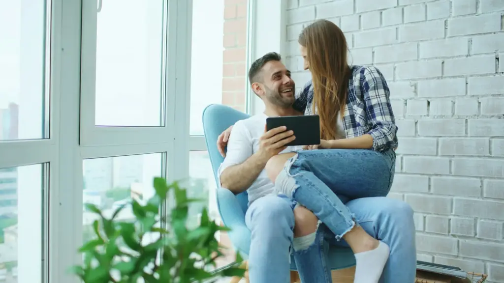 Couple sitting togeather in a chair, looking at their finances on a tablet.